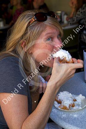 Woman eating a beignet at Cafe Du Monde in the French Quarter of New Orleans, Louisiana, USA.