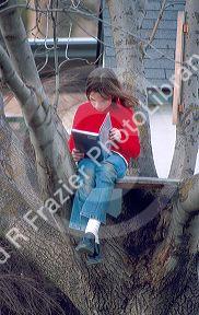 Ten-year-old girl reading book in tree house.  MR