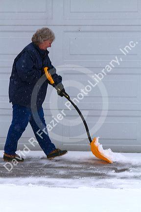 Woman shoveling winter snow of off a driveway in Boise, Idaho, USA.