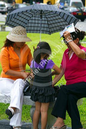 Women shading themselves from the hot sun with an umbrella at the Plaza Mayor or Plaza de Armas of Lima, Peru.