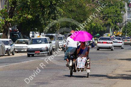 Woman shading herself with an umbrella while riding in a trishaw in (Rangoon) Yangon, (Burma) Myanmar.