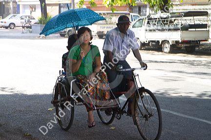 Woman shading herself with an umbrella while riding in a trishaw in (Rangoon) Yangon, (Burma) Myanmar.