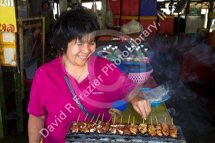 Woman grilling satay at an open air market on the island of Ko Samui, Thailand.