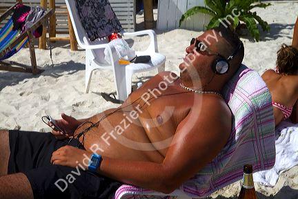 Man wearing head phones while sun tanning at Chaweng beach on the island of Ko Samui, Thailand.