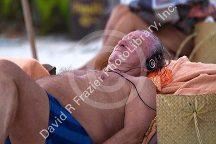 Elderly man wearing head phones sun bathing at Chaweng beach on the island of Ko Samui, Thailand.