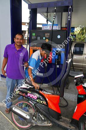 Gas station attendent filling up a motor scooter on the island of Ko Samui, Thailand.
