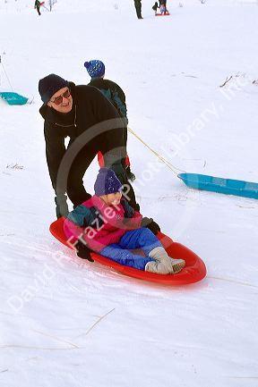Grandfather pushing his grandaughter on sled in the snow.