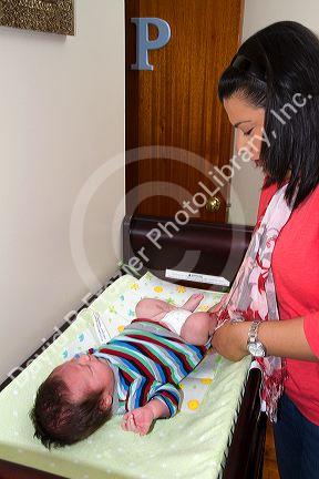 Hispanic mother with infant son on a changing table in Boise, Idaho, USA. MR