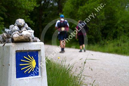 Pilgrims walk near a marker along the Camino De Santiago, the Way of St. James pilgrimage route, Navarra, Spain.