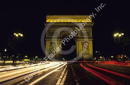 Night view of the Arc de triomphe in Paris, France with streaked lights from passing automobiles.