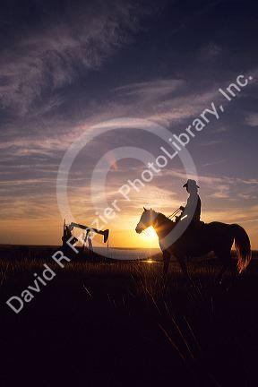 A silhouetted cowboy on horseback with an oil well in the background in Williston, North Dakota.
