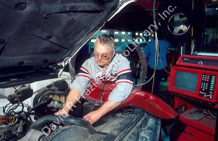 An auto mechanic working on a car using a computer monitor to analyze the engine.