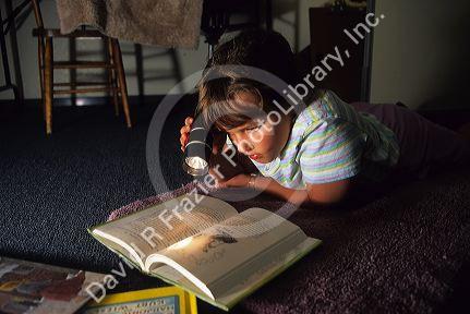 A young girl reading a book with a flashlight.