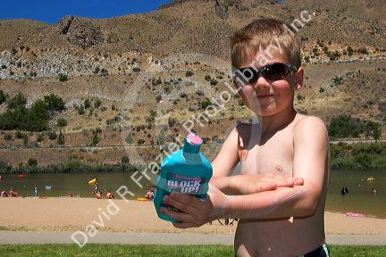Five year old boy applying sunblock while at the beach. Sandy Point near Boise, Idaho. MR
