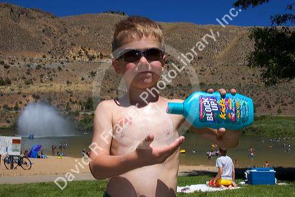 Five year old boy applying sunblock while at the beach. Sandy Point near Boise, Idaho. MR