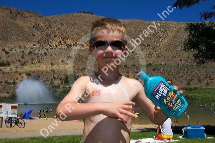Five year old boy applying sunblock while at the beach. Sandy Point near Boise, Idaho. MR