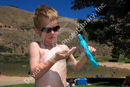 Five year old boy applying sunblock while at the beach. Sandy Point near Boise, Idaho. MR