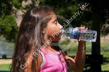 Young hispanic girl drinking water out of a bottle.