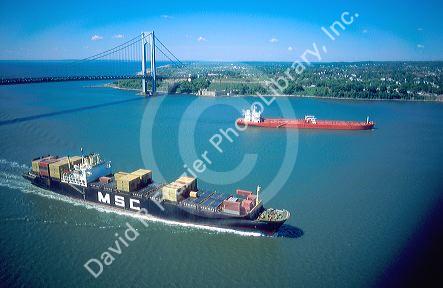 Container ship entering New York Harbor with tanker ship and Verrazano Narrows Bridge in background.