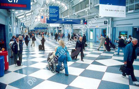 Chicago's O'hare airport terminal.  Handicapped passenger and other travelers walking with bags and suitcases.