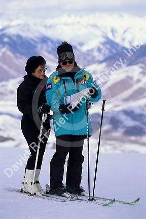 A couple snow skiing with sun glasses and nylon waterproof clothing.