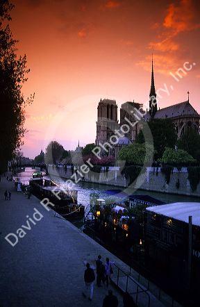 A view of the Notre Dame Cathedral at sunset in Paris, France with boats along the River Seine.