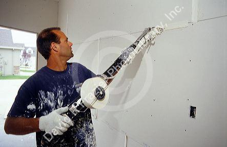 A dry wall  worker uses a drywall tape applicator called a bazooka to tape joints and seams.