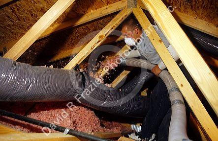 A worker insulates the attic space around a duct in a new home with blown in insulation.