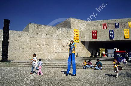 A man on stilts and children in front of the Museum of Mayan Cultures, Mexico City, Mexico.