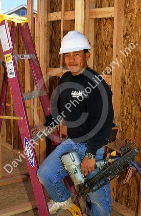 Portrait of a hispanic carpenter wearing a hard hat and holding a nail gun. MR