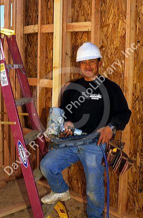 Portrait of a hispanic carpenter wearing a hard hat and holding a nail gun. MR