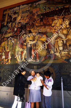 A mexican family stands in front of a Diego Rivera mural at the National Palace in Mexico City, Mexico.