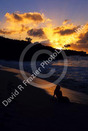 A woman silhouetted on the beach at sunset in Hawaii.