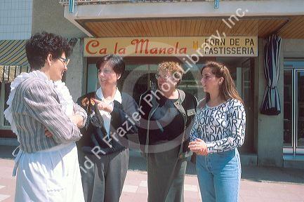 Women meet and talk in Spain in front of bakery.