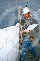 Mason using level, to plumb up course with wall.