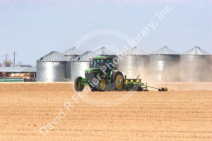 A tractor planting corn  crop in Canyon County, Idaho.  HEat waves reflecting off grain bins.