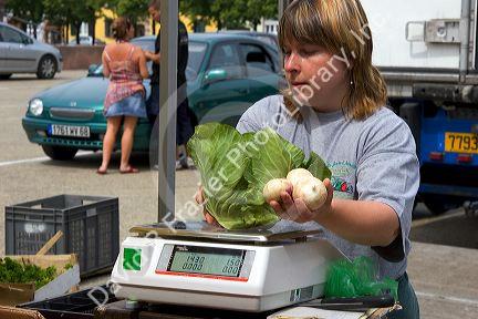 A woman weighs lettuce and radish at an open air market in Neuf-Brisach, France.