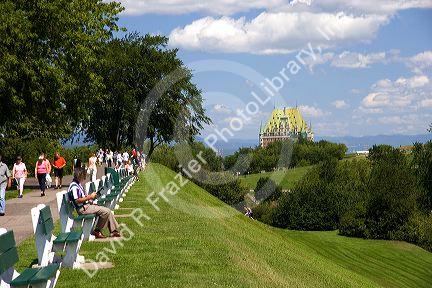 People sit on benches and walk on a path with the Chateau Frontenac in the background at Quebec City, Quebec, Canada.