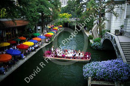 Visitors on a boat tour and people dining along the River Walk in San Antonio, Texas.