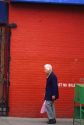 An elderly woman walks in front of a red brick wall in Chinatown, San Francisco, California.