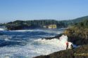 A couple stands watching waves crash on the rocks in Boiler Bay on the Oregon Coast.