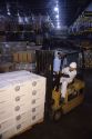 A worker using a forklift to move a pallet of cheese being stored in a refrigerated warehouse.