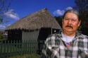 Ted Billie, a seminole Miccosukee Indian, standing in front of a chopekcheke traditional thatched roof dwelling in Florida. (model released)