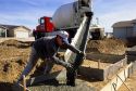 A worker wearing rubber gloves pours concrete into forms for a new home foundation, Idaho.