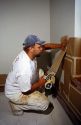 A painter uses a masking tape applicator to mask off portions of the wood work and wall he does not wish to have paint on.