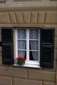 A window framed with green shutters and flowers on the Ligurian Coast of Italy.