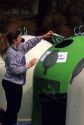 A woman depositing colored glass bottles into a recycling bin at a recycle center.