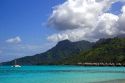 Grass hut bungalows and sailboat anchored in the lagoon on the island of Moorea.