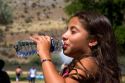 Young hispanic girl drinking water out of a bottle.