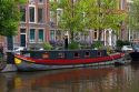 Canal boat docked in front of row houses along a canal near the Amstel River in Amsterdam, Netherlands.